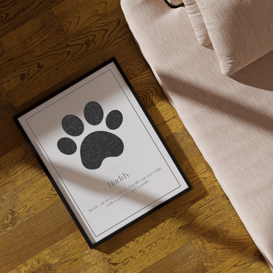 Pet paw print art in black frame on wooden floor beside beige sofa, capturing cozy home decor.