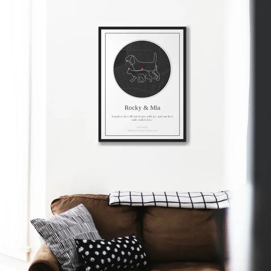 Framed personalized pet map gift hanging above a cozy couch with pillows.