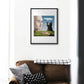 Art print depicting a philosophical scene with a cat, human face, and nature elements, framed and displayed above a sofa.