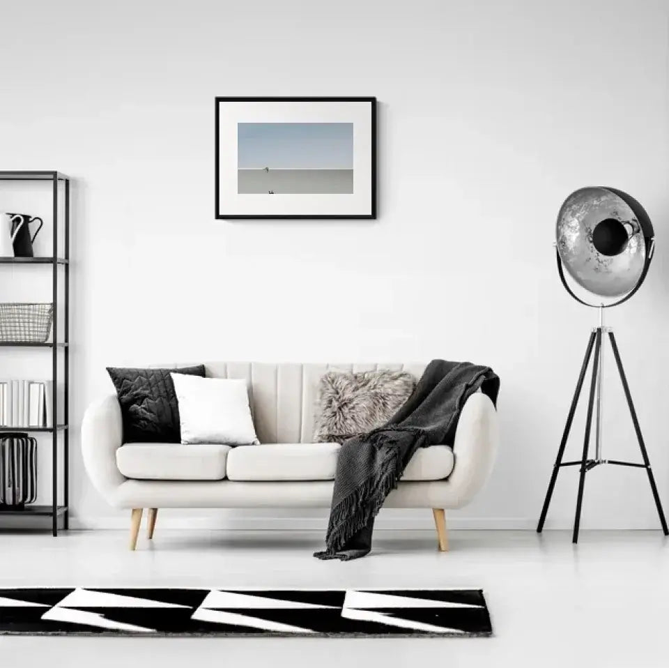 Modern living room with white sofa, geometric rug, and framed art print on the wall, featuring minimalistic decor elements.