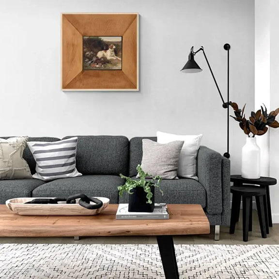 Art print of a dog and pheasant hangs in a modern living room with gray sofa and wooden coffee table.