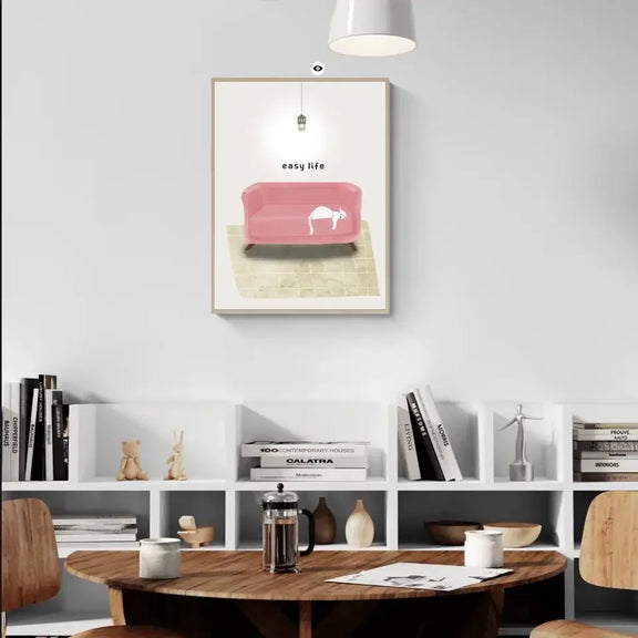 Cozy living room with "Cat Nap Art Print" featuring a relaxed cat on a pink couch, adding tranquility to home decor.